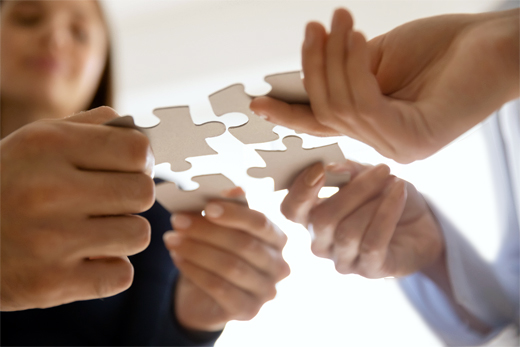 Mehrere Hände halten zusammenpassende Puzzleteile